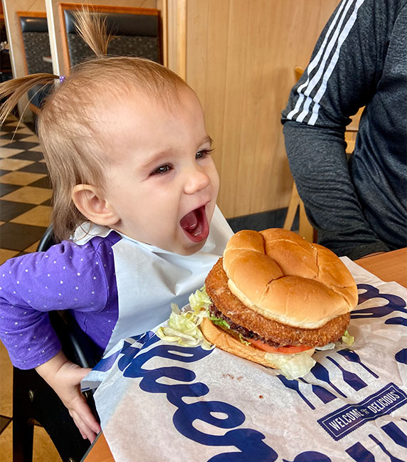 A baby smiles with a CurderBurger.
